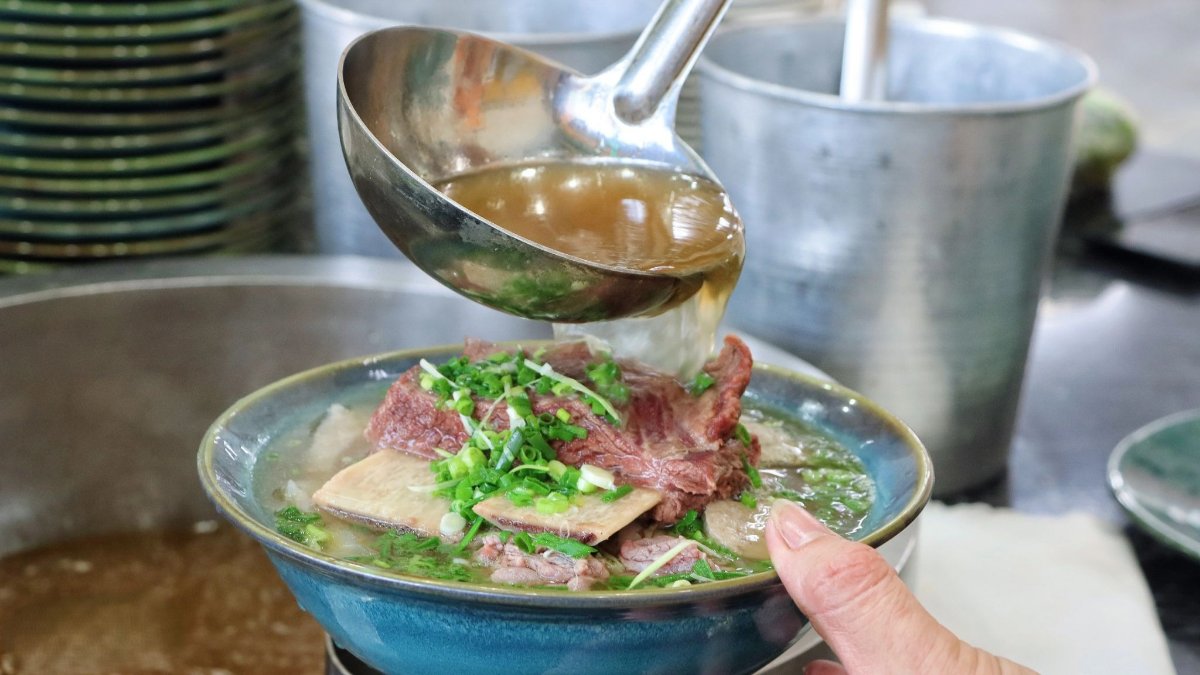 Hot broth being poured over a bowl at Pho Dong Lien, bringing out the aroma of beef and scallions